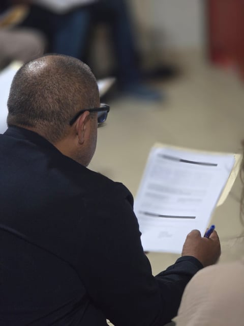 Persona usando lentes leyendo un documento en un ambiente de taller grupal